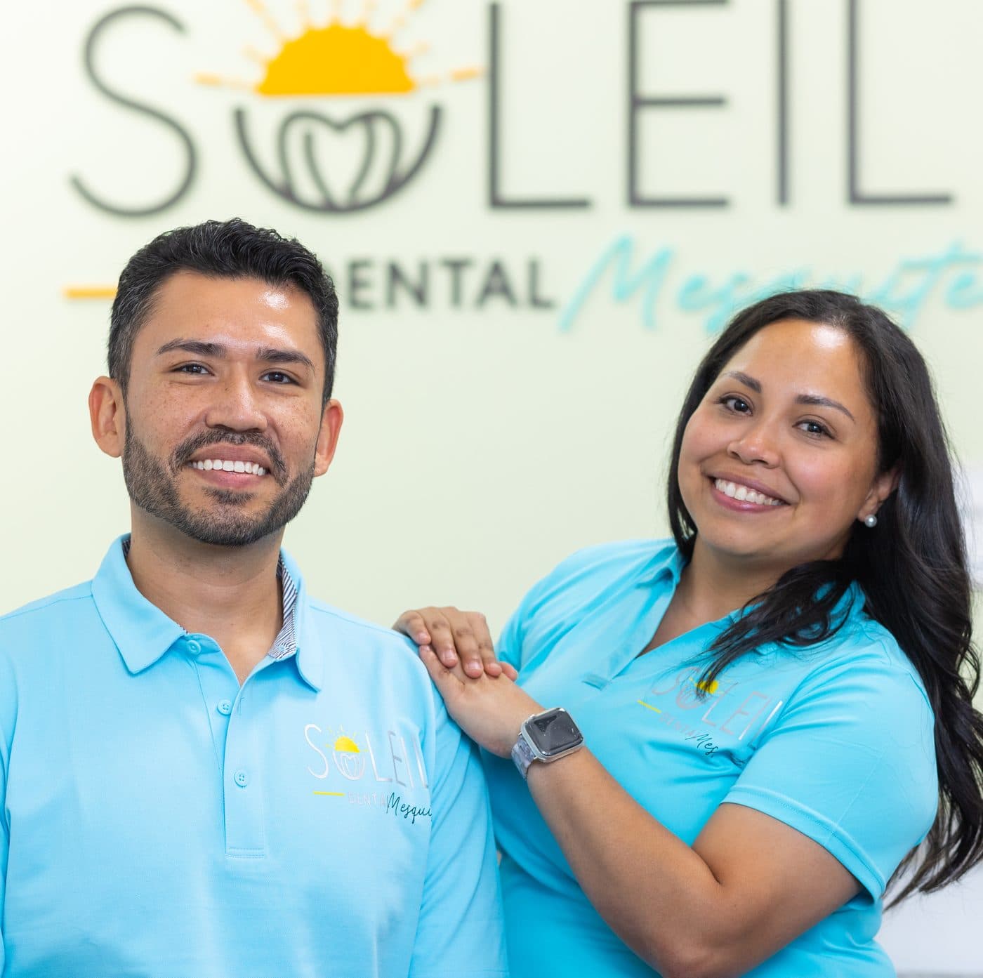 Dr. Diana Vazquez and Dr. Jose Aldana, the dentists who own Soleil Dental Mesquite, in front of the office logo wall