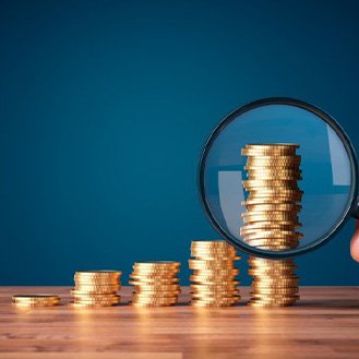 Magnify glass looking at increasingly taller stacks of coins